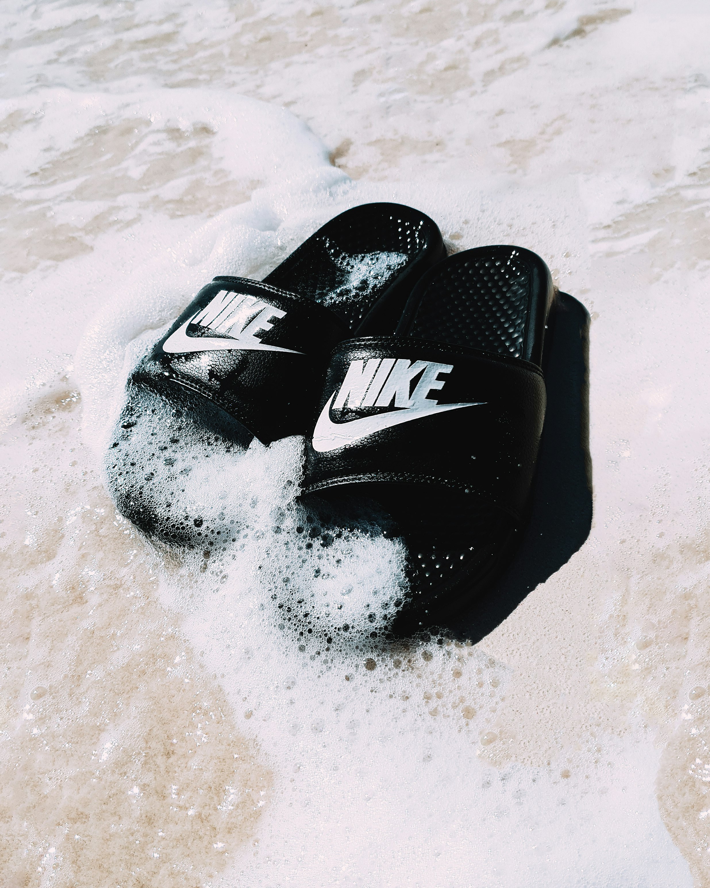 black and white nike flip flops on white sand